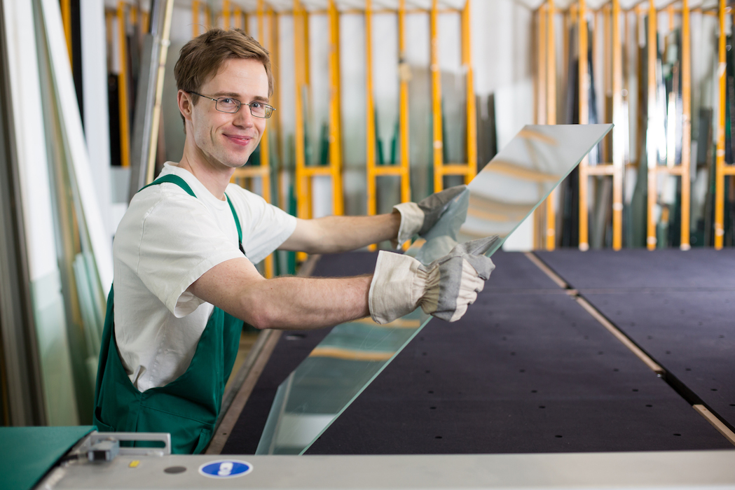 junger mann in einer werkstatt hält eine glasscheibe