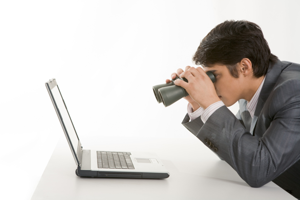 mann schaut durch fernglas auf laptop