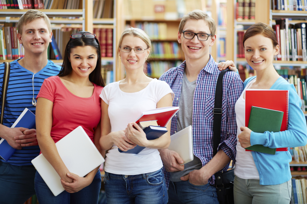 fünf junge studenten stehen in bibliothek und lächeln