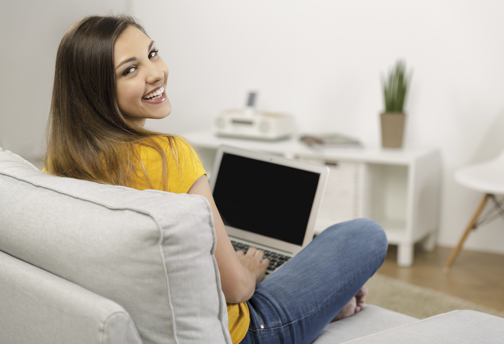 junge frau sitzt auf weissem sofa und hat laptop auf ihrem schoss 