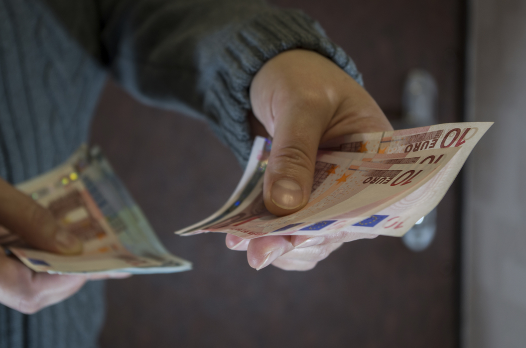 eine person in grauerm kleidung reicht euroscheine aus seiner hand